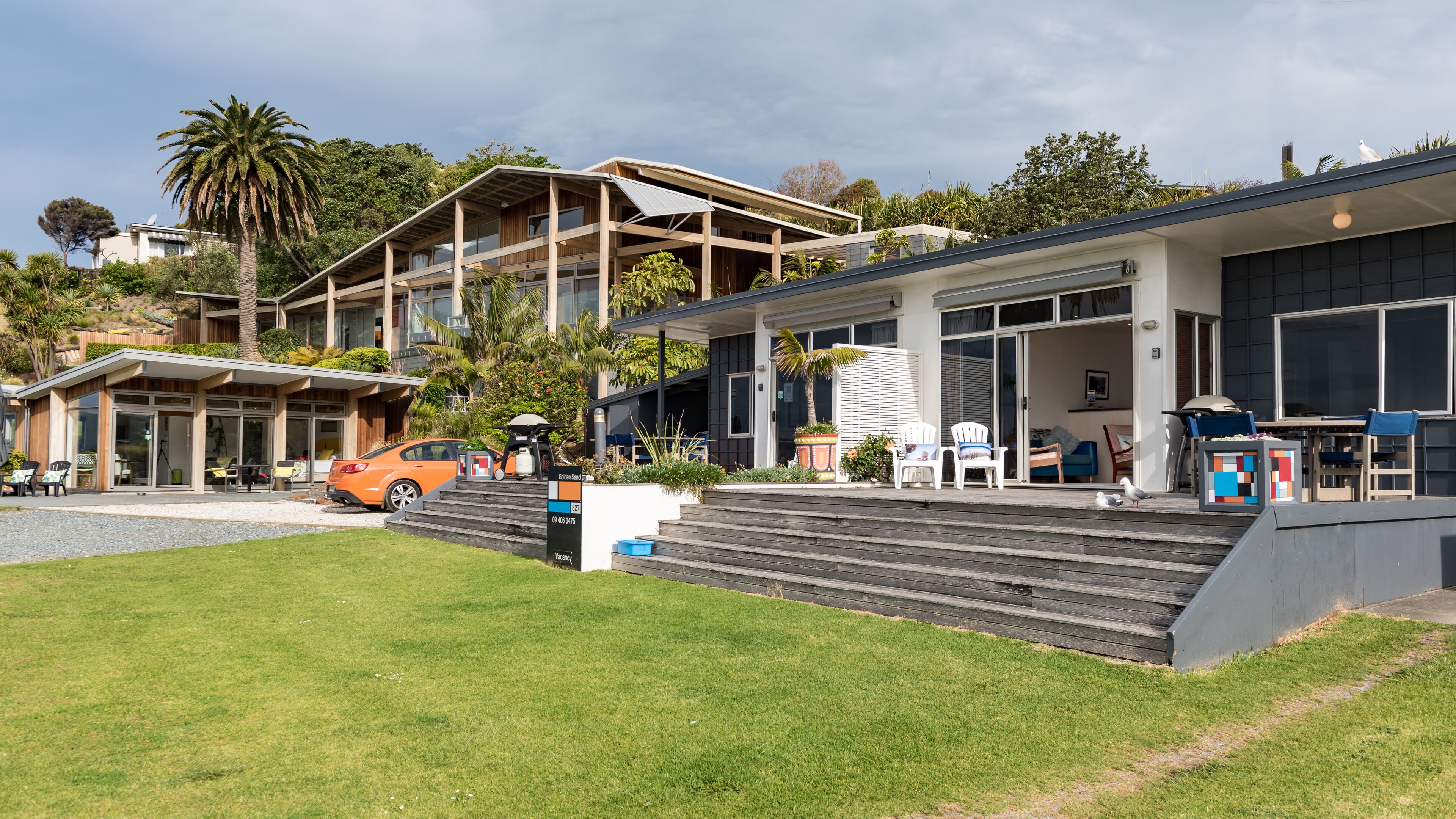 A modern two-story building with a flat roof, large windows, and a covered outdoor seating area with chairs and tables.