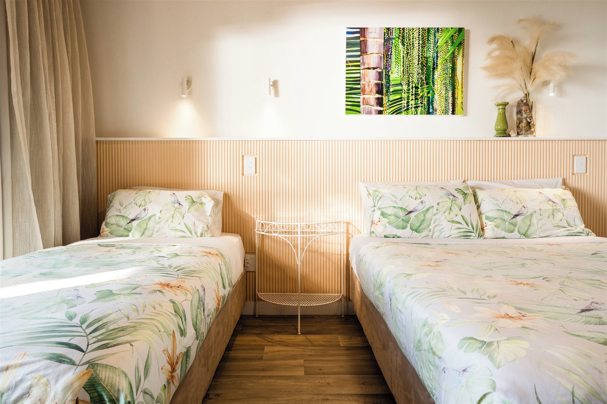 Habitación de hotel con dos camas, suelo de madera, lámpara fijada a la pared y un adorno colgante en la pared.