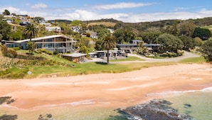 Une propriété située sur la côte, comprenant plusieurs maisons modernes, une plage et un paysage vallonné en arrière-plan.