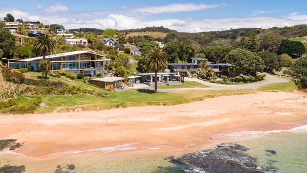 A coastal property with multiple modern houses, a beach, and a hilly backdrop. - Cable Bay Stays – Golden Sand and Driftwood Beachfront Accommodation (Cable Bay)