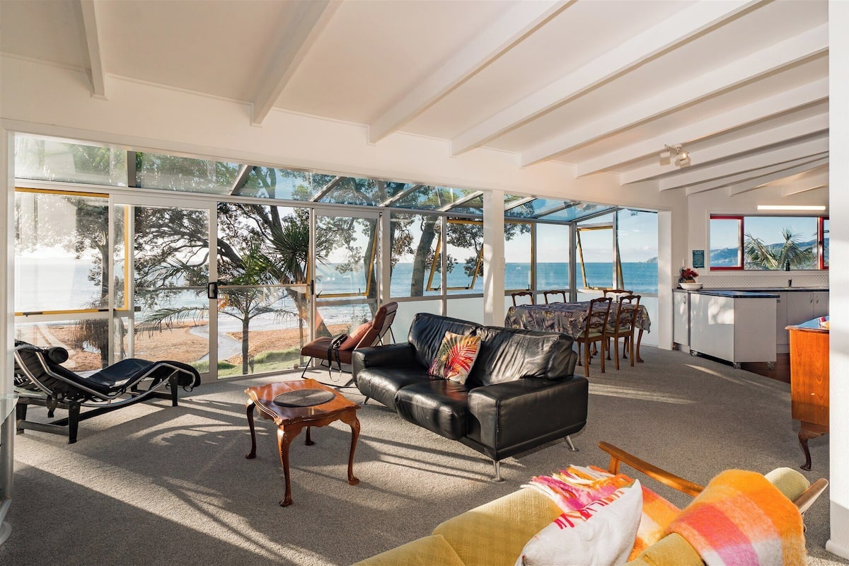 A spacious living area with a large glass wall offering a view of the beach and sea.