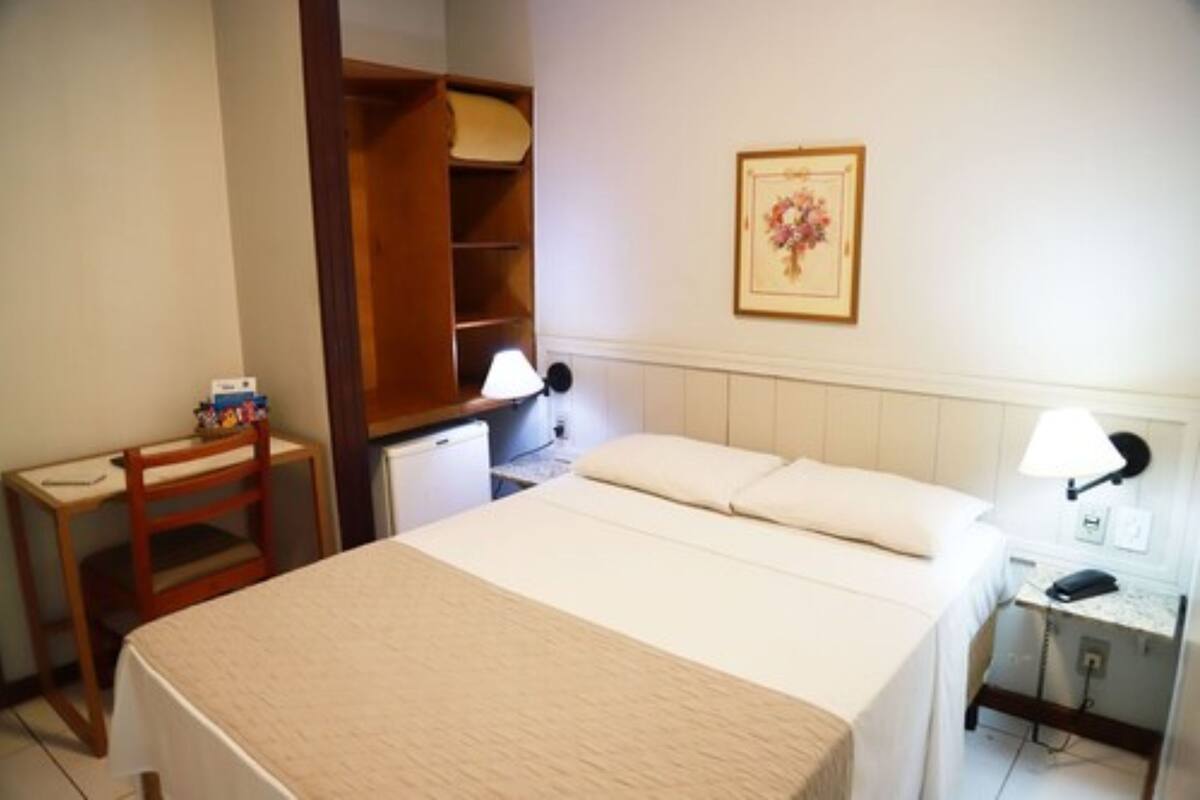 Een hotelkamer met een bed, een bureau, een stoel, een kledingkast en een nachtkastje met een lamp.