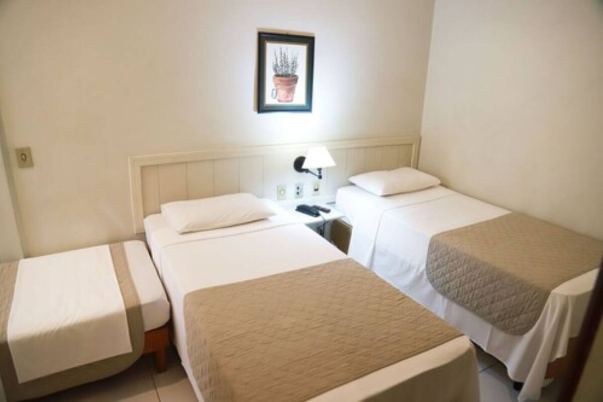 Een hotelkamer met twee eenpersoonsbedden, een nachtkastje met een lamp en een lijst aan de muur.