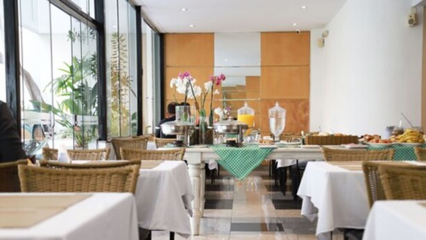 Un restaurant avec des tables dressées pour le service, un espace buffet proposant des plats et des boissons, et une vue sur l’extérieur grâce à de grandes fenêtres.