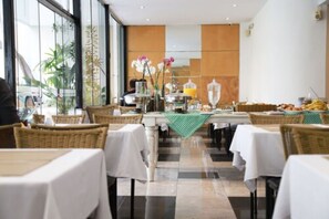 A restaurant with tables set for dining, a buffet area with food and drinks, and a view of the outside through large windows.