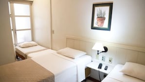 Une chambre d’hôtel avec deux lits simples, un bureau avec une lampe, un téléphone et un tableau encadré au mur.