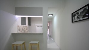 Un pasillo estrecho con una zona de cocina a la izquierda, que incluye una encimera y dos taburetes de madera.