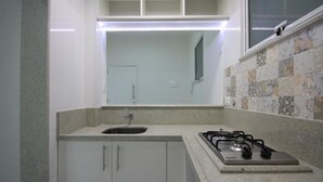 Una cocina compacta con estufa a gas integrada, un lavamanos y armarios blancos.