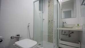Un baño moderno con ducha de vidrio, inodoro blanco y lavamanos con espejo.