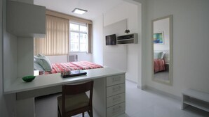 Un dormitorio con cama, escritorio, silla, espejo y ventana.