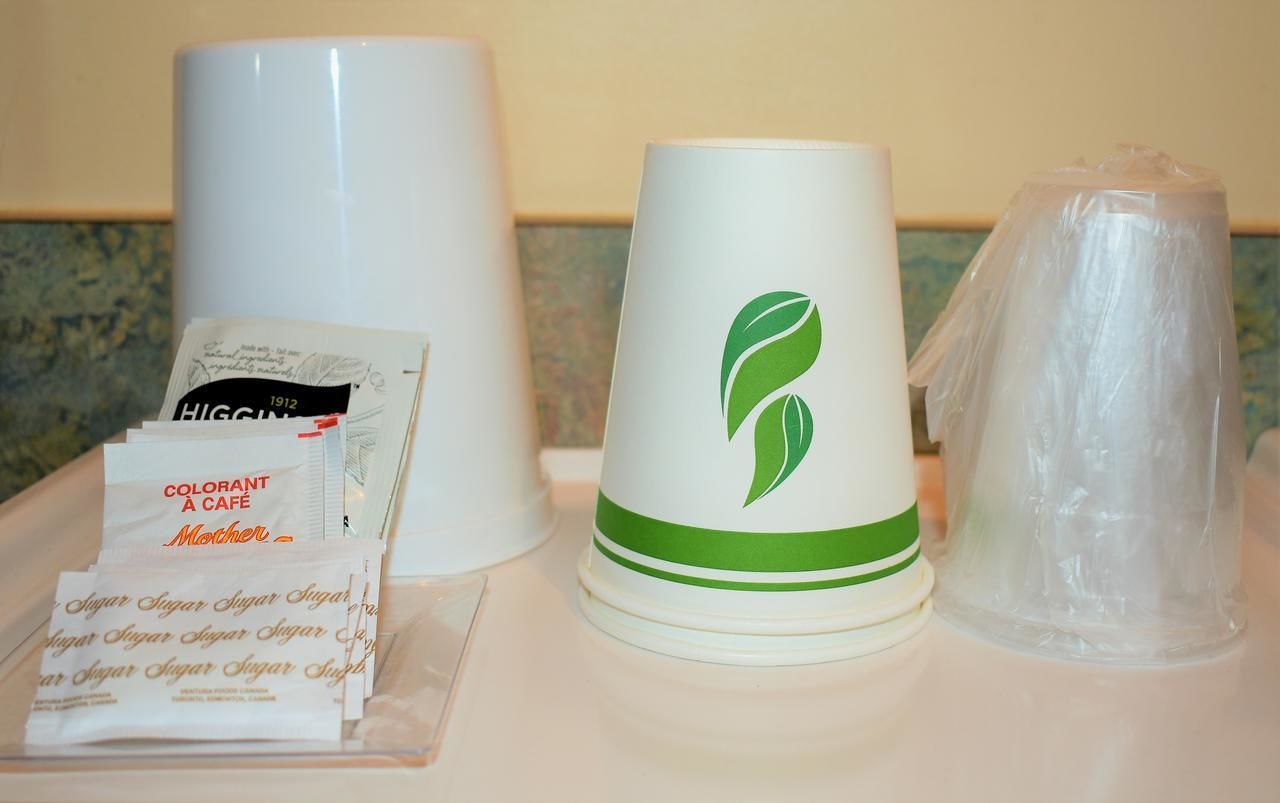 Ein Tablett mit einer weißen Tasse, einer grün-weißen Kaffeetasse, Zuckerportionen und einer Plastiktüte.