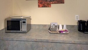 A kitchen with a microwave, a tray with cups and a kettle, and a wall-mounted painting of a sunset over the ocean.