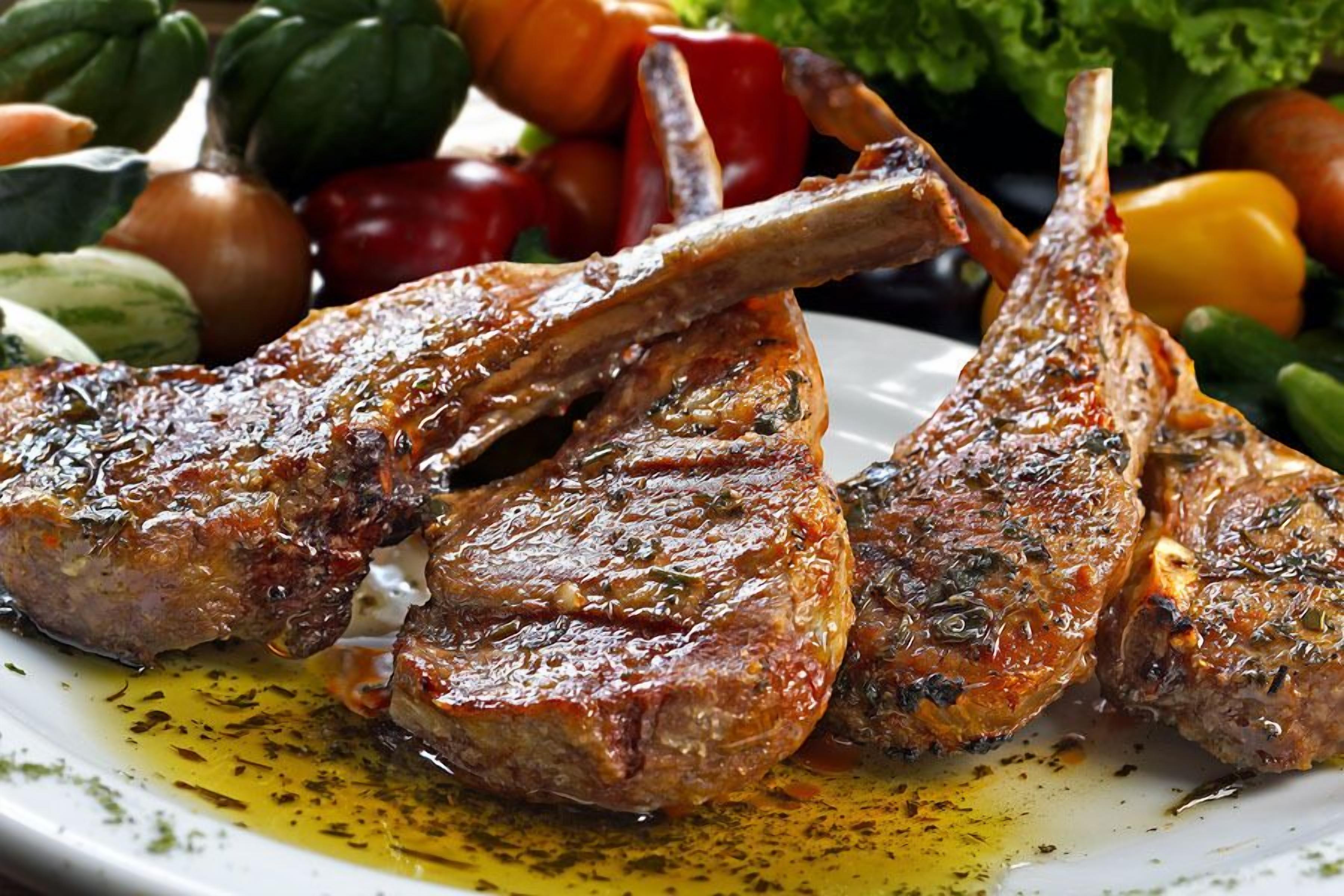 A plate of grilled lamb chops with a garnish of herbs and olive oil.
