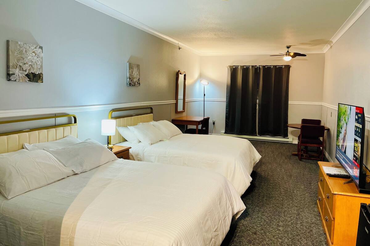 Une chambre d’hôtel avec deux lits, un bureau, une chaise, une télévision et un ventilateur de plafond.