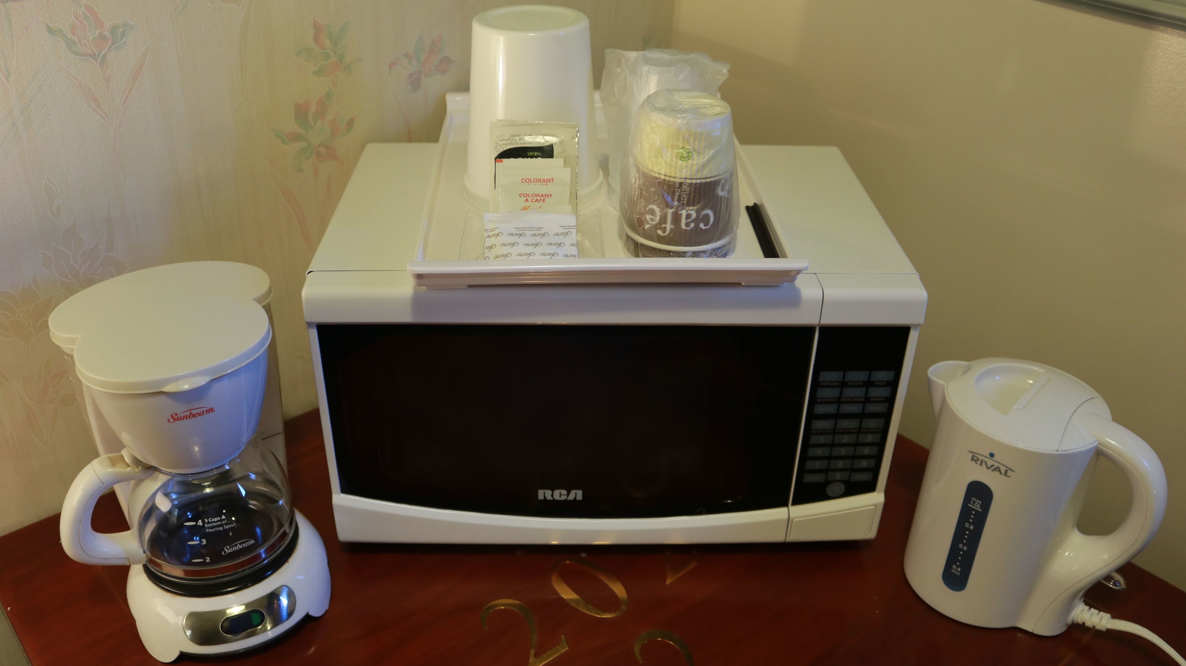 A kitchen area with a coffee maker, a microwave, and a coffee pot on a wooden table.