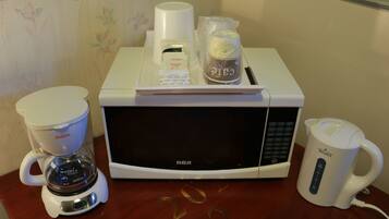 A kitchen area with a coffee maker, a microwave, and a coffee pot on a wooden table.