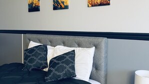 A neatly made bed with a dark green comforter and patterned pillows, a grey headboard, and a bedside table with a lamp and phone.