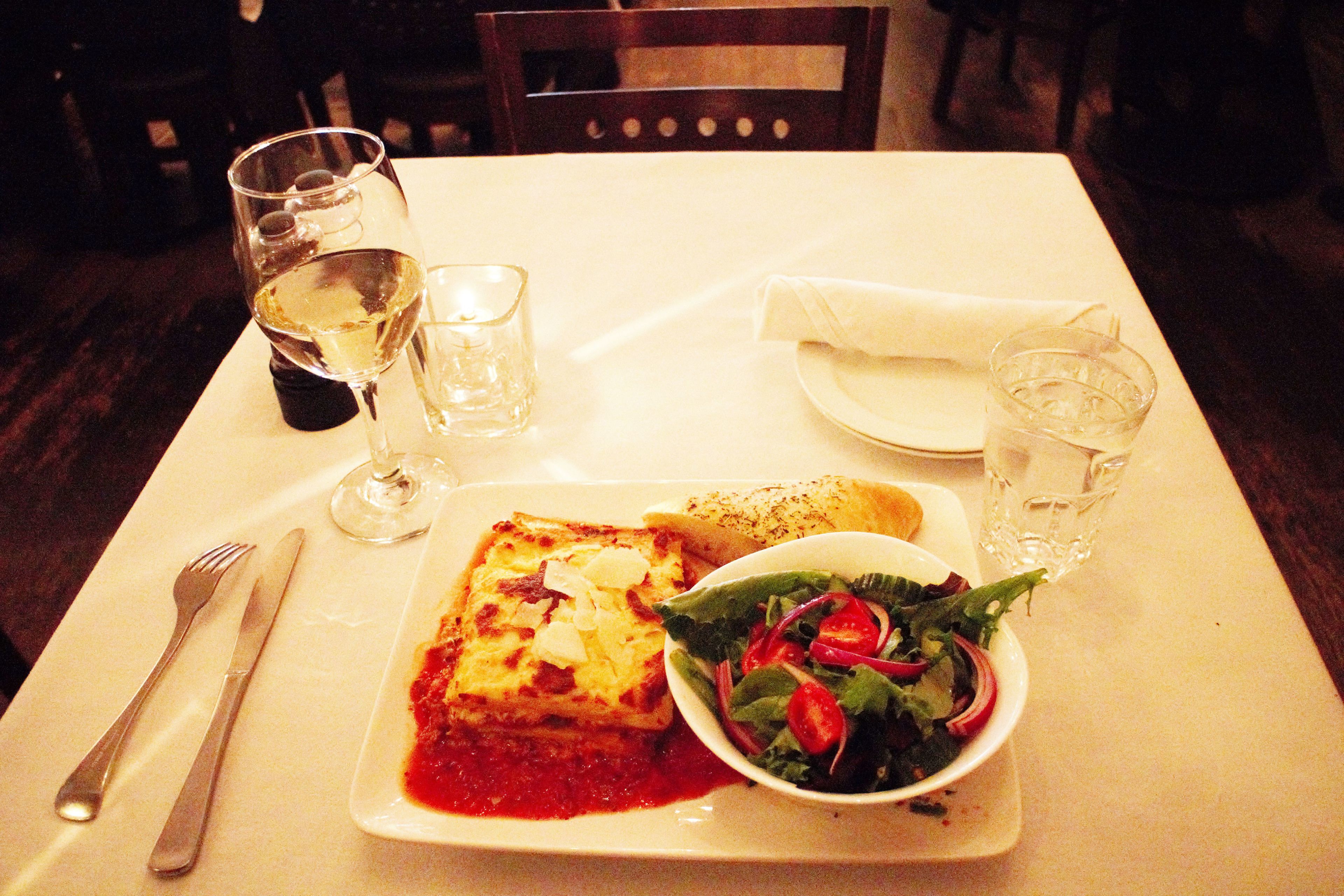 A dining table with a plate of food, a glass of water, and a glass of wine.