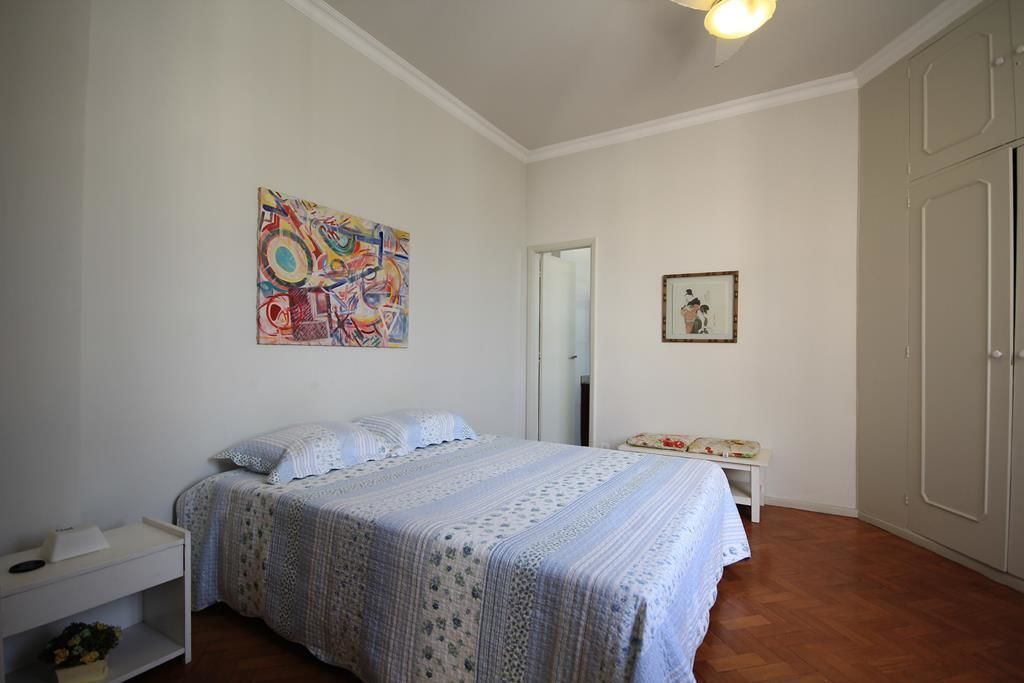 A bedroom with a bed, a bedside table, a chair, a wardrobe, and a painting on the wall.
