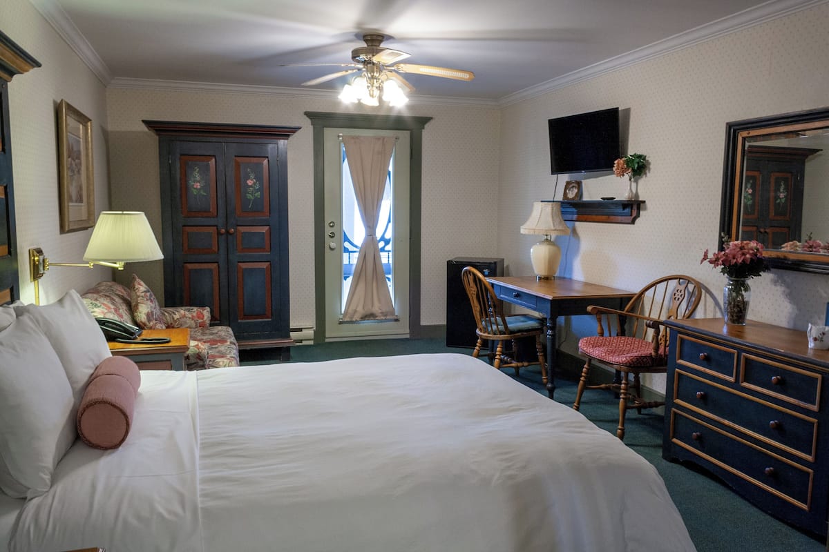 A hotel room with a bed, desk, dresser, and a ceiling fan.