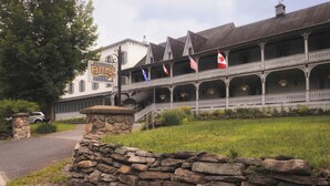 A building with a stone wall entrance, a sign reading 'ENTERTAINMENT,' and multiple balconies with flags. - Auberge Lakeview Inn (Lac-Brome)