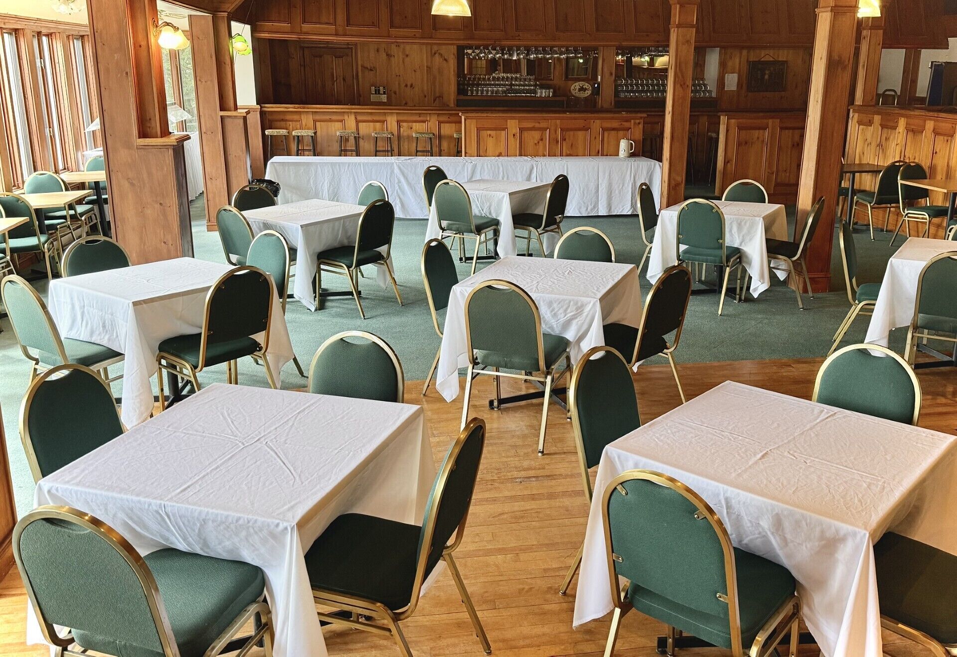 A restaurant with multiple tables and chairs, wooden paneling, and a bar area.