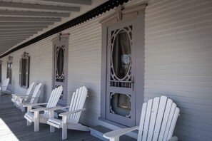 Una hilera de sillas Adirondack blancas en un porche, con un edificio blanco al fondo.