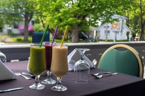 Una mesa con tres bebidas en vasos, una copa de vino y cubiertos sobre un mantel.