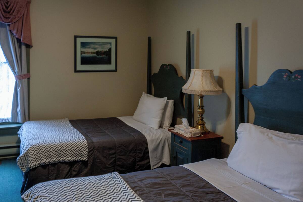 A hotel room with two beds, a nightstand with a lamp, a framed picture on the wall, and a window with curtains.