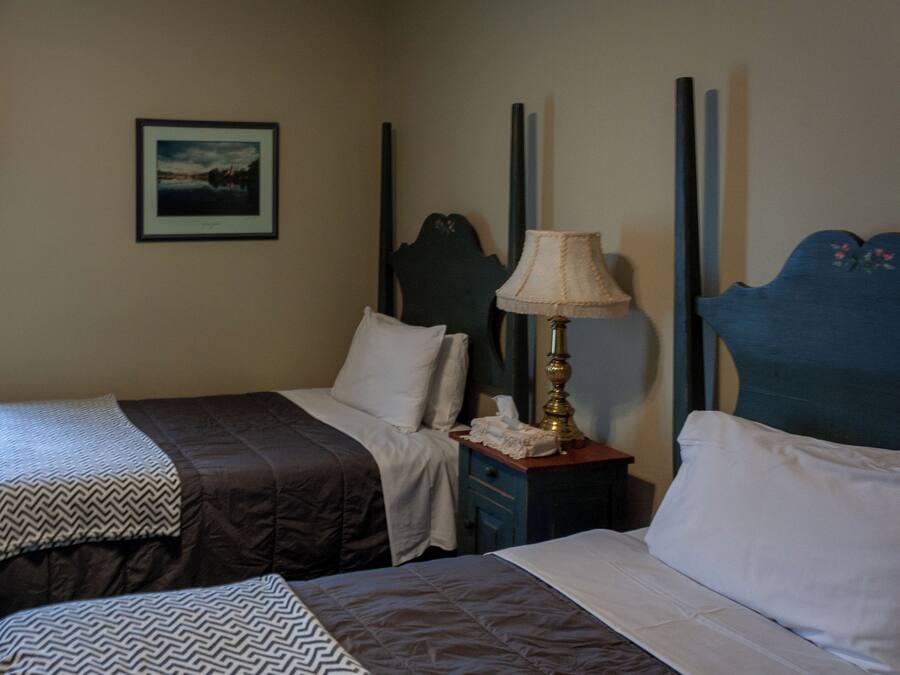 Habitación de hotel con dos camas, una mesita de noche con lámpara, un cuadro en la pared y una ventana con cortinas.