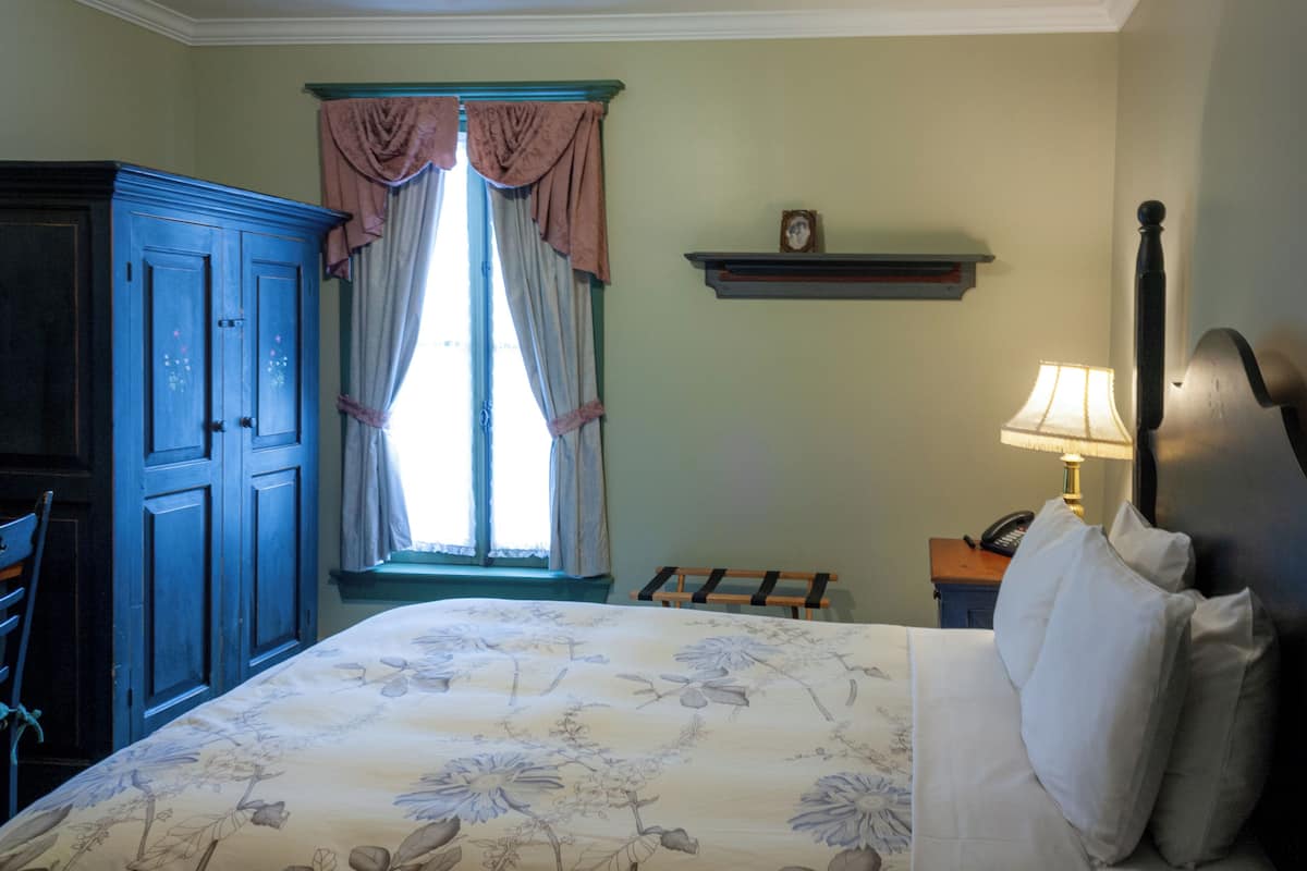 A bedroom with a bed, a dresser, a nightstand, a lamp, and a window with curtains.