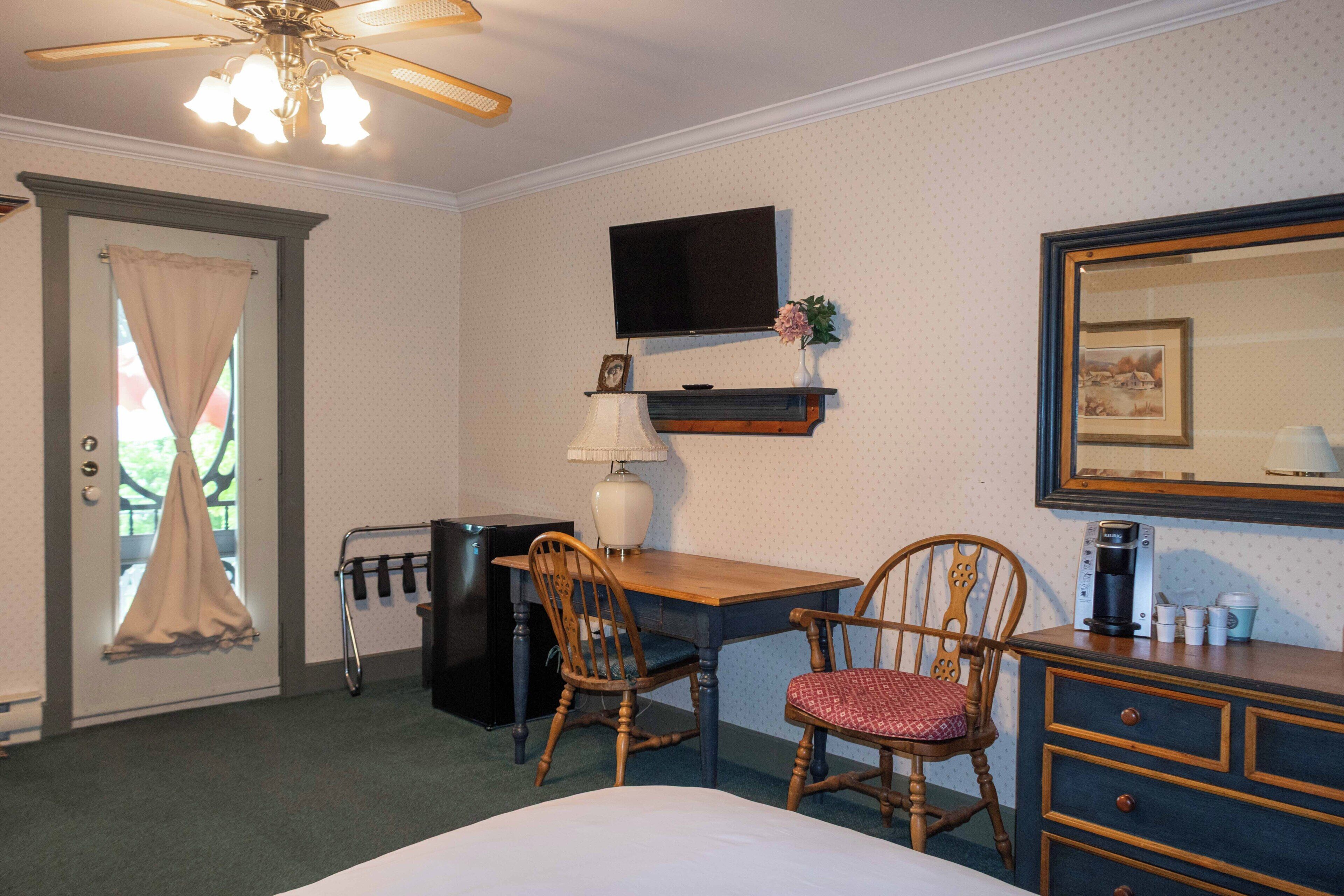 Habitación de hotel con cama, escritorio, dos sillas, televisor, cafetera y cómoda.
