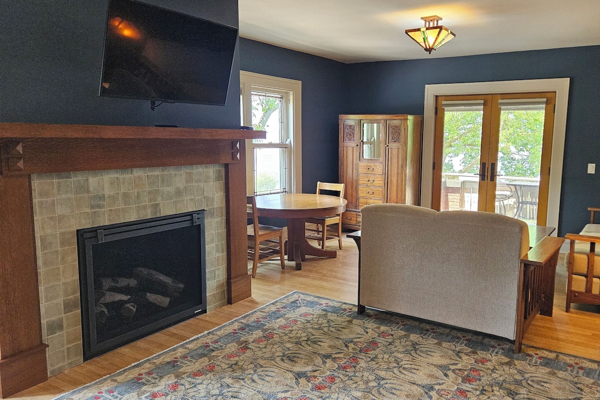 A living room with a fireplace, a dining area, and a view through a glass door.