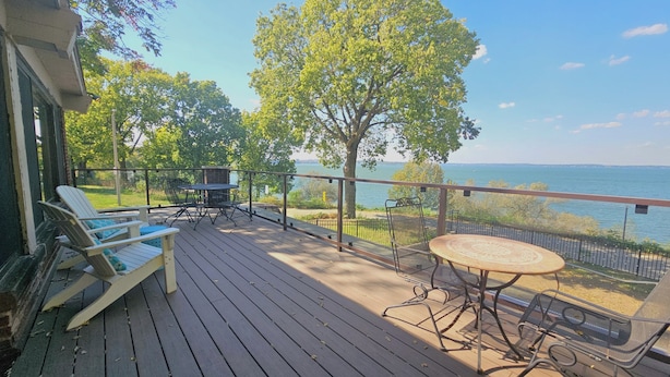 A wooden deck with outdoor furniture, a view of the lake, and a railing.