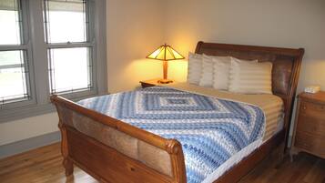 A wooden bed with a blue and white quilt, a bedside lamp, and a nightstand.