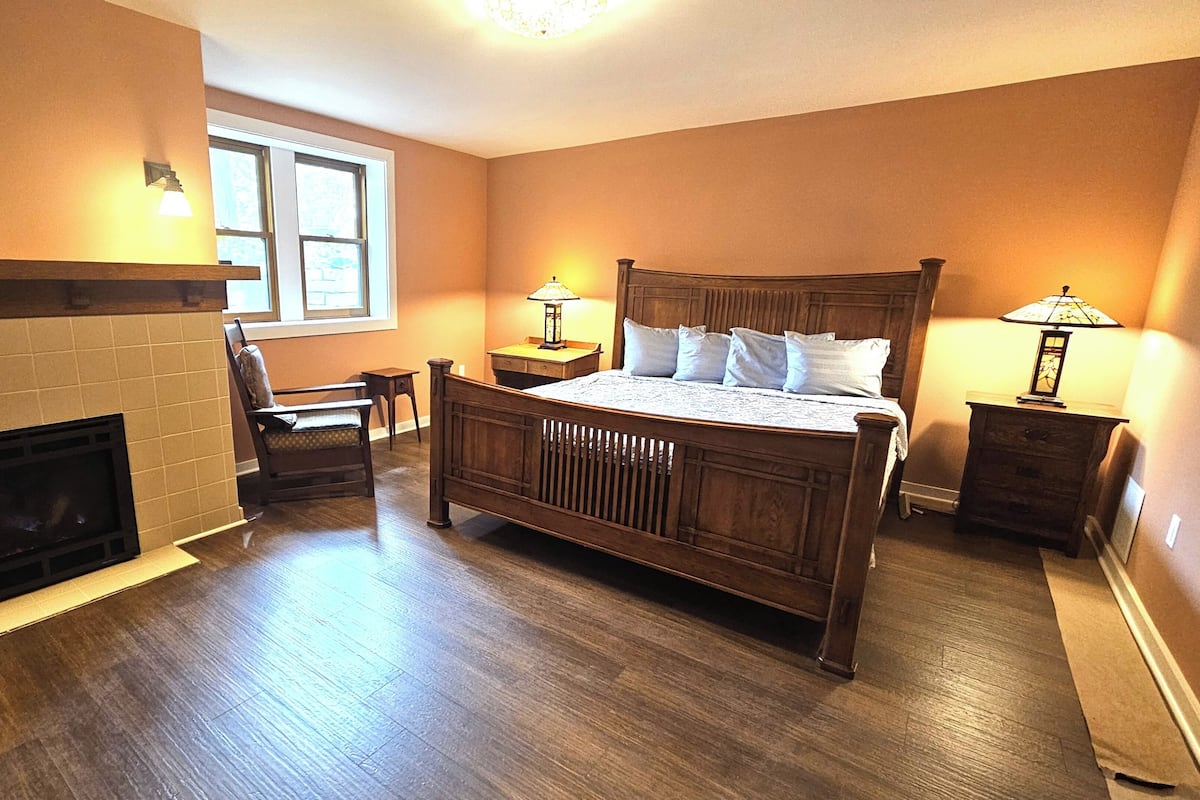 A bedroom with a wooden bed, a fireplace, and two bedside lamps.