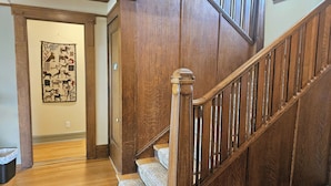 A wooden staircase with a handrail, leading to a room with a wooden door and a wall-mounted artwork.