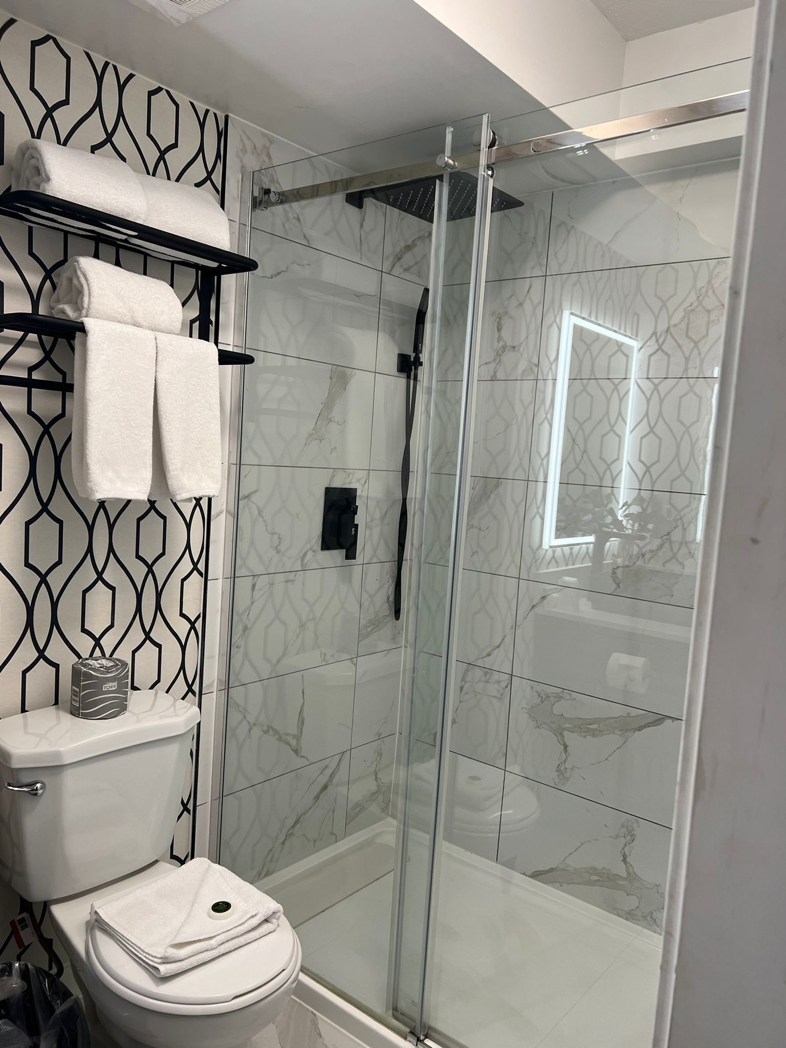 Un baño moderno con ducha de vidrio, azulejos de mármol y un perchero con toallas dobladas.
