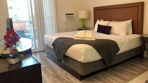 A hotel room with a bed, a nightstand, a lamp, and a view of the outdoors. - The Spot (Nanaimo)