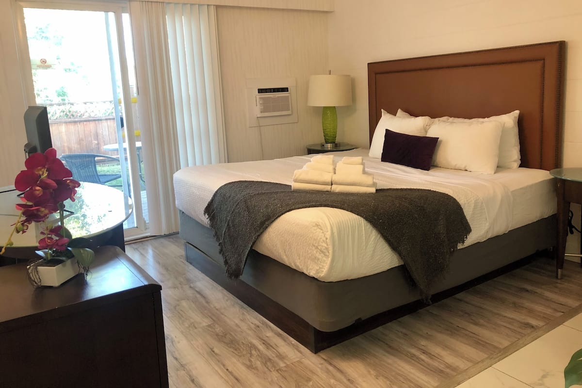 Habitación de hotel con cama, mesita de noche, lámpara y vistas al exterior.
