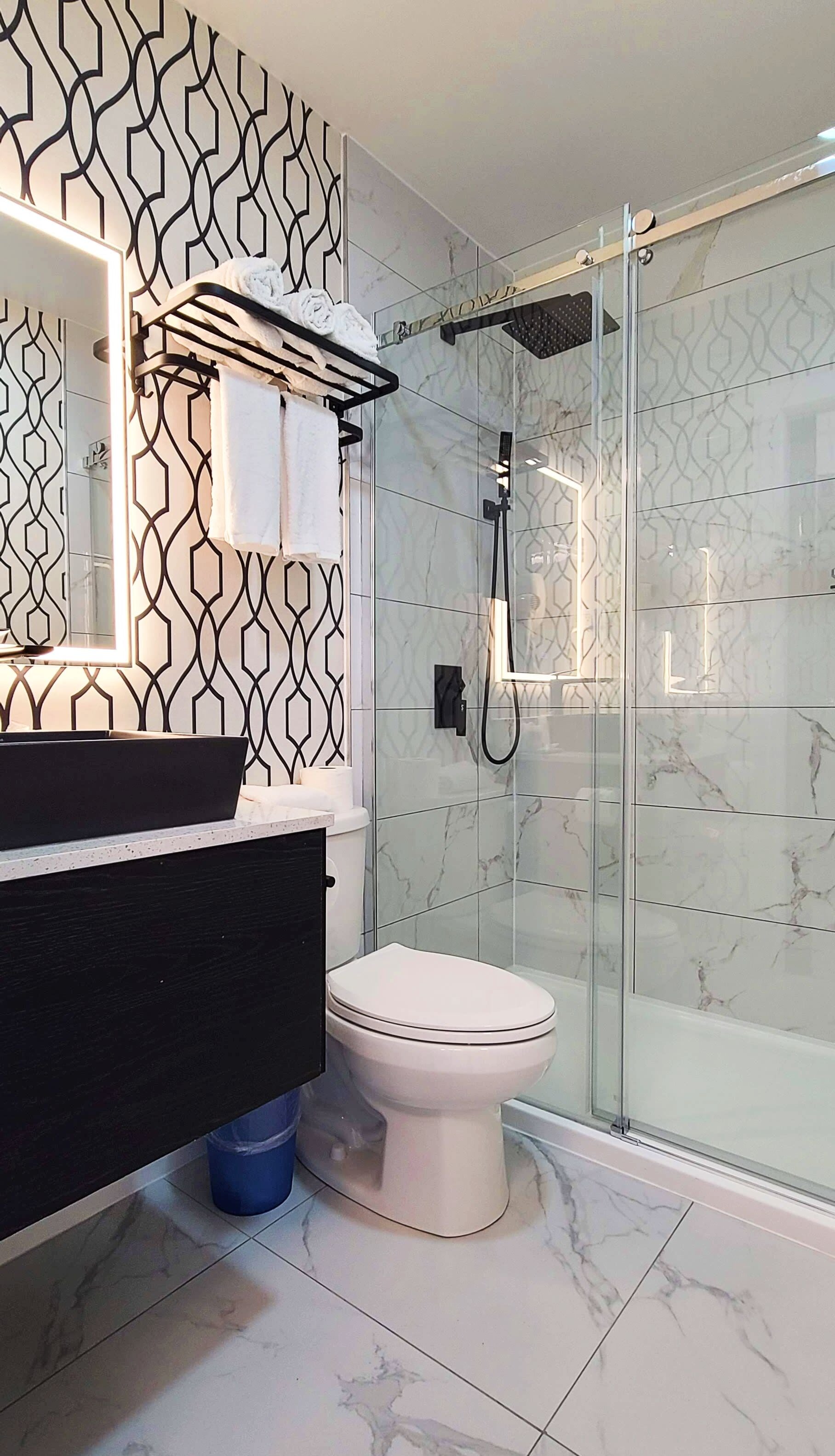 Une salle de bain moderne avec un mur à motifs noir et blanc, une douche en verre et des toilettes blanches.