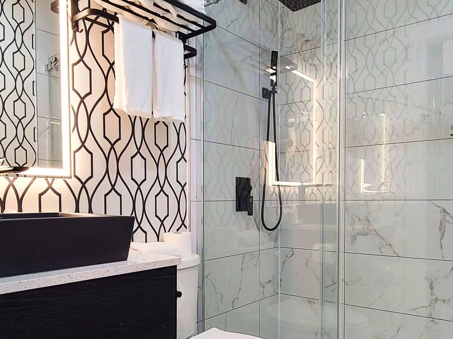 A modern bathroom with a black and white patterned wall, a glass shower enclosure, and a white toilet.