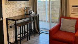 A room with a TV mounted on the wall, a wooden table with two stools, a red sofa, and a sliding glass door leading outside. - The Spot (Nanaimo)