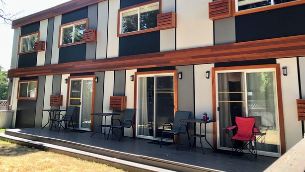 A modern two-story building with a flat roof, large windows, and a covered outdoor seating area with tables and chairs. - The Spot (Nanaimo)
