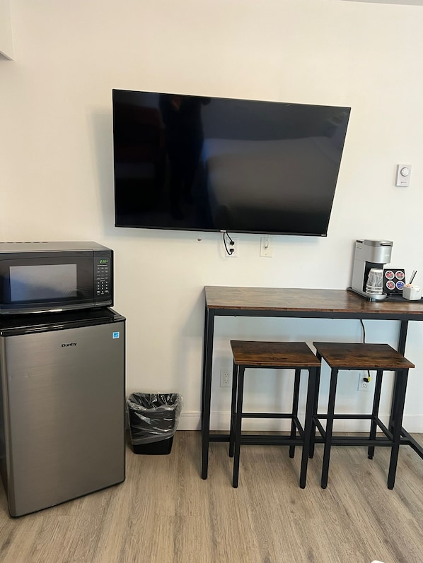 Una kitchenette compacta con microondas, refrigerador y un televisor de pantalla plana montado en la pared.