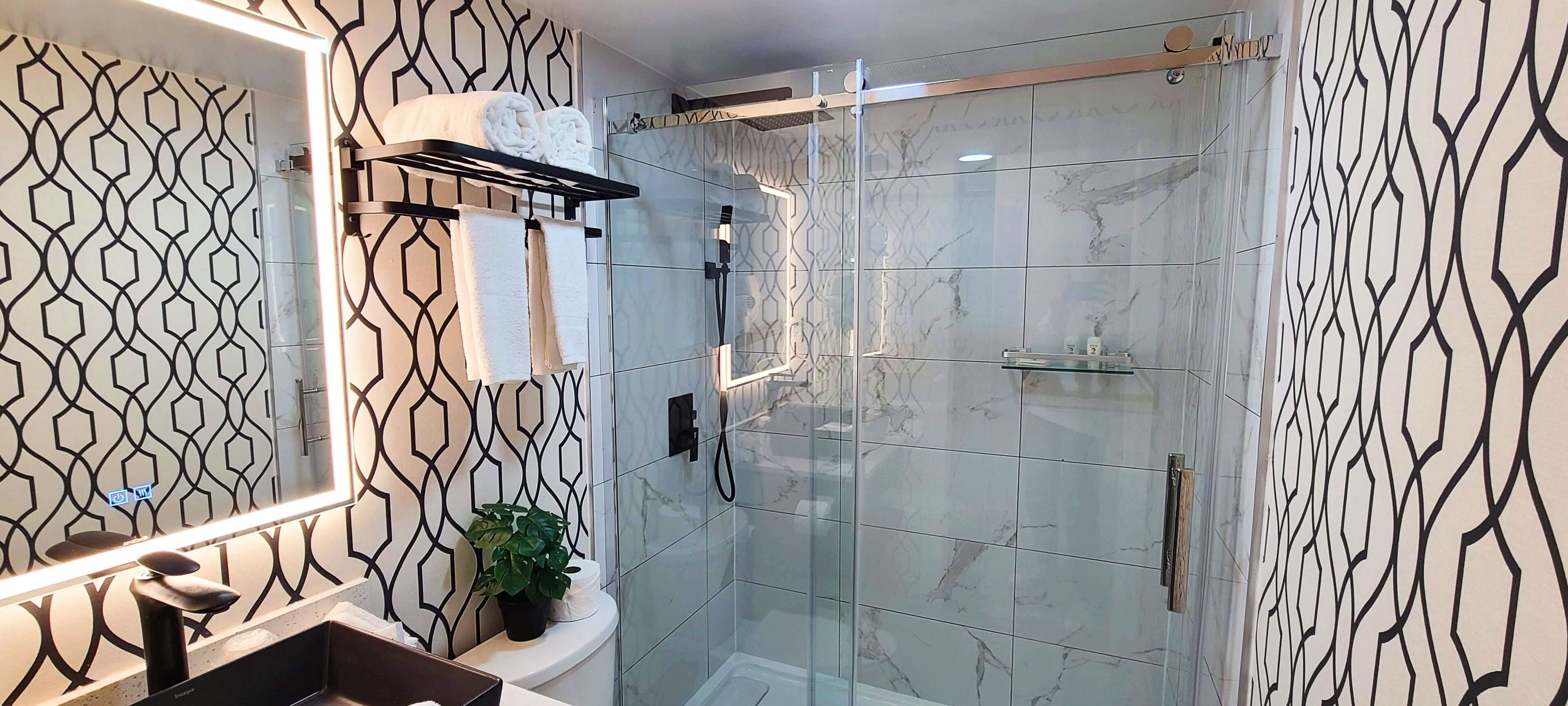 Un baño moderno con ducha envuelta en vidrio, un lavamanos con espejo y un perchero para toallas.
