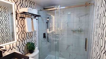 Un baño moderno con ducha envuelta en vidrio, un lavamanos con espejo y un perchero para toallas.