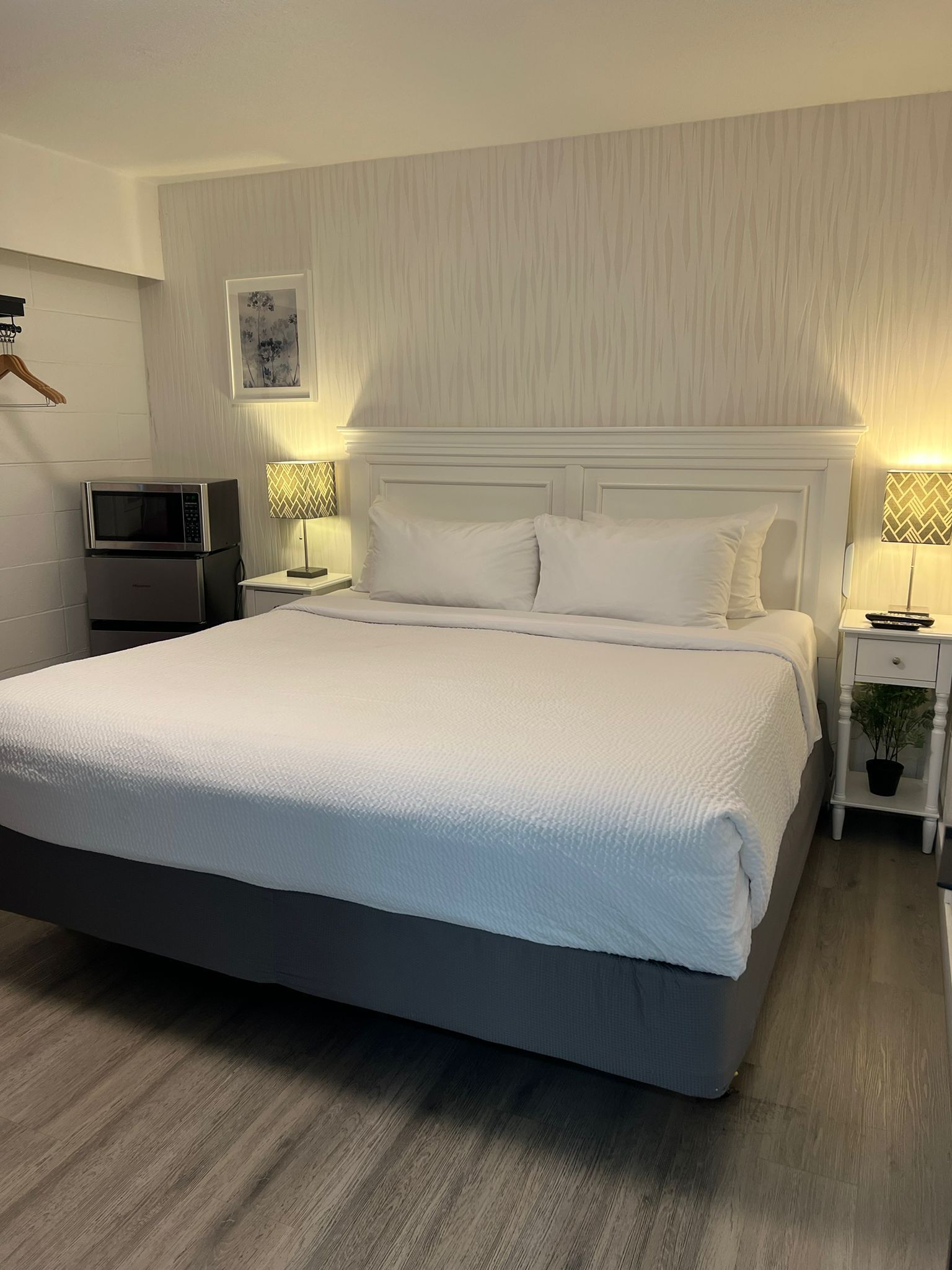A neatly arranged hotel room with a large bed, a microwave, a small table, and a nightstand with a lamp.