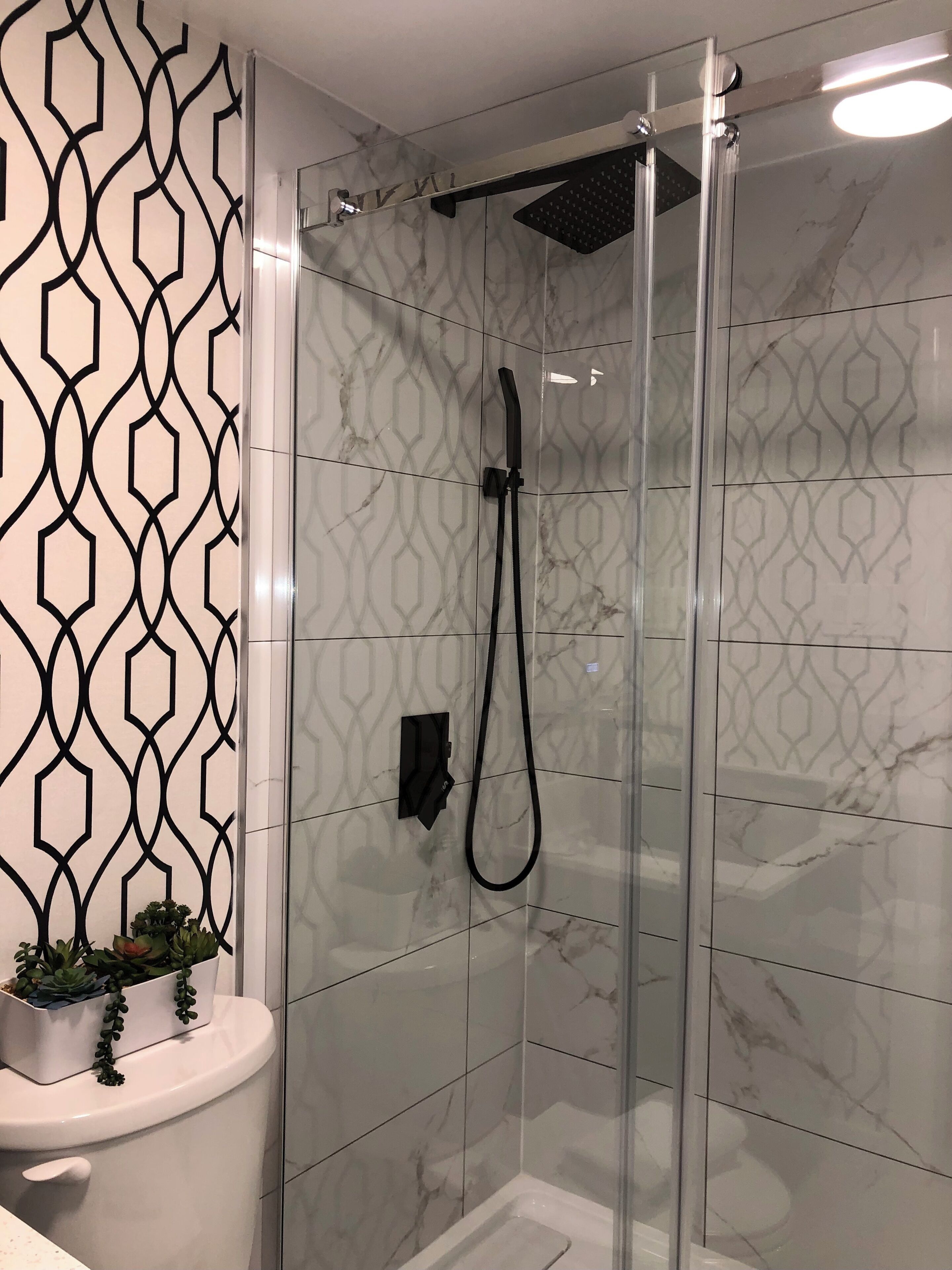 Un box de ducha moderno con puerta de vidrio, un cabezal de ducha manual y un panel de control en la pared.