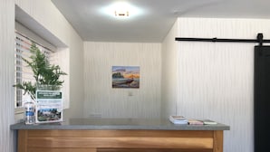 A reception desk with a wooden panel design, a framed painting of a sunset, and a sign indicating special offers for hotel guests. - The Spot (Nanaimo)